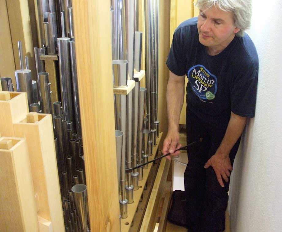 Figure 3 — An organ technician tuning a flue chorus by ear at the pipe tops, working at the instrument's stated tuning temperature — flues and reeds are set against each other only after the room is thermally…