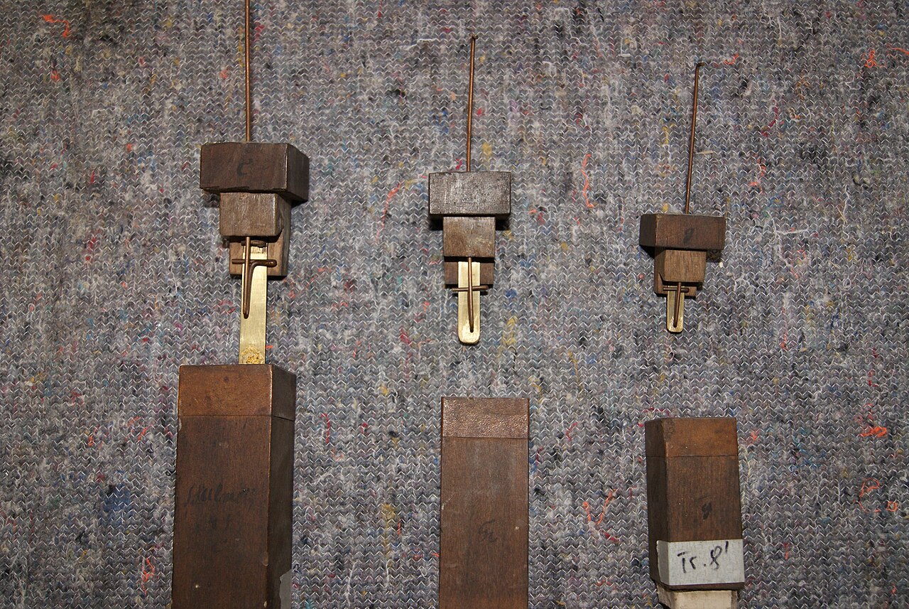 Figure 2 — A reed pipe taken apart: resonator, block, boot, and the reed assembly with brass tongue, shallot, wedge and tuning wire laid out — the parts that turn steady wind into a pitched buzz.