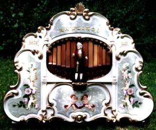 Figure 3 — A finished, decorated John Smith 26-note "Universal" organ — carved and painted case, pipe fronts, and cranked drive — the end state this eleven-volume series builds toward.
