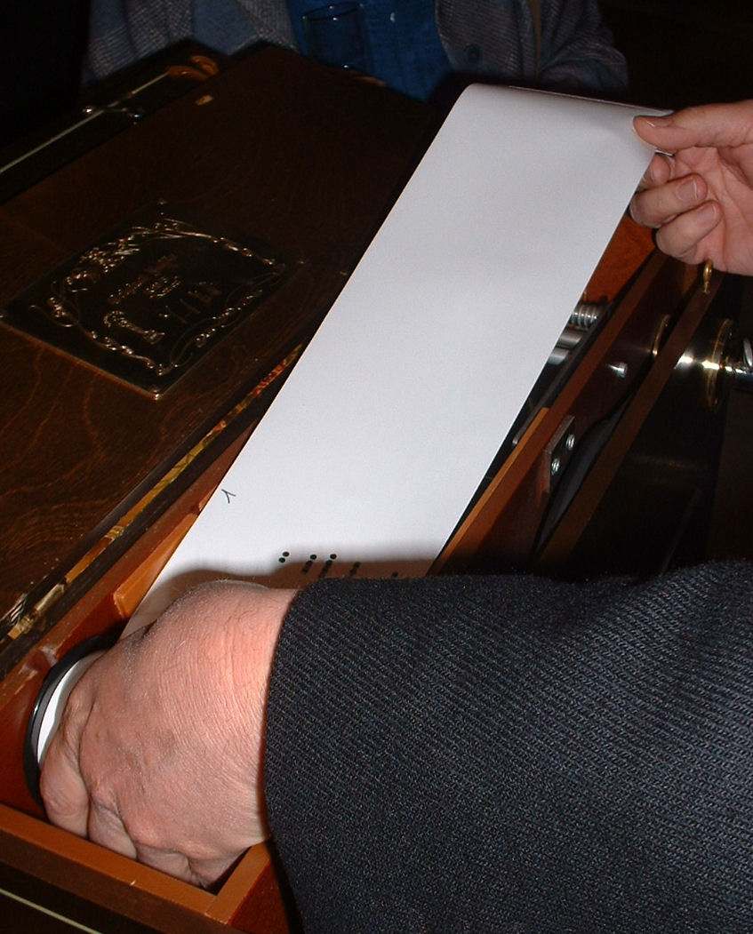 Figure 2 — A punched paper music roll for a 20-note crank organ wound on its reel, showing the round note holes, held-note slots, and edge control tracks.